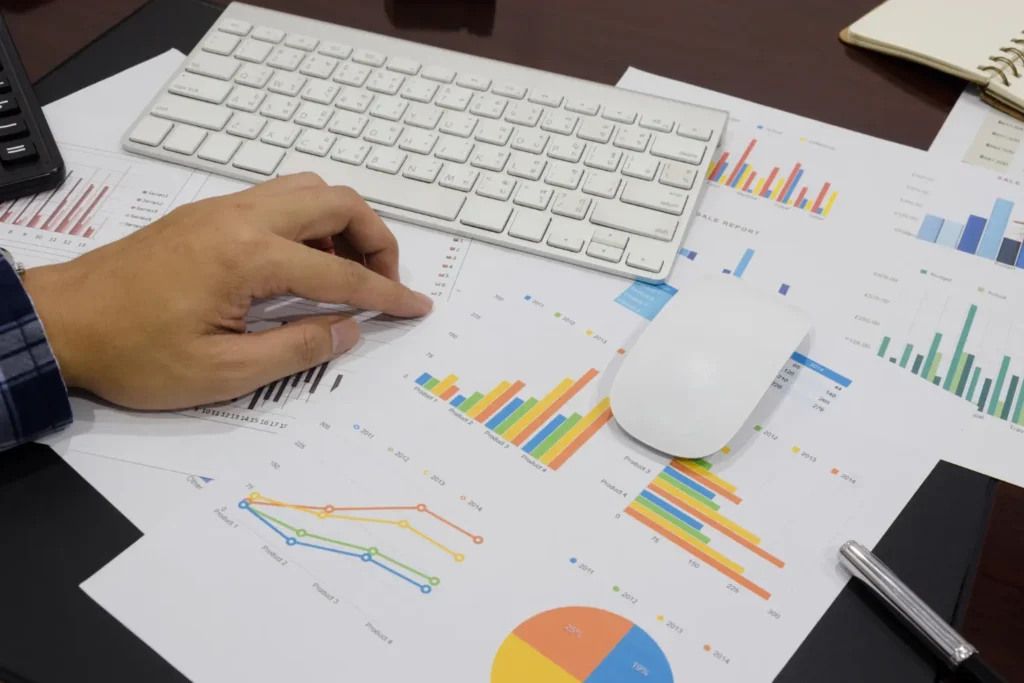 Person analyzing data charts and graphs on a desk, with keyboard and mouse, for business insights and performance review.